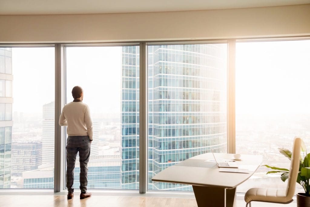Business owner looking out window in high-rise office, reflecting on future exit strategy