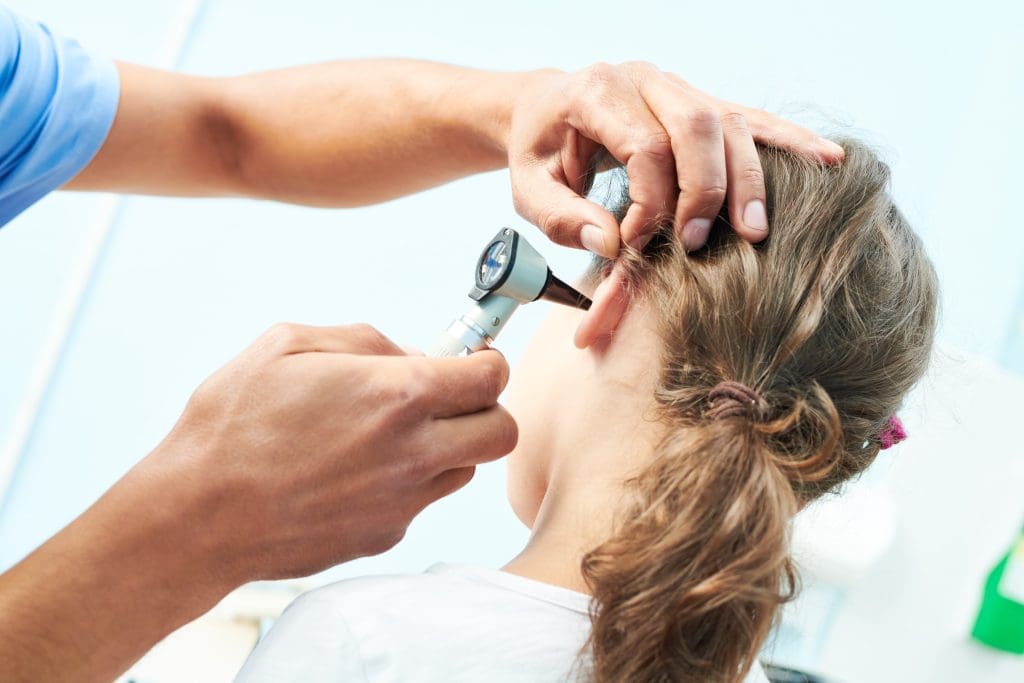 A healthcare professional uses an otoscope to examine a young girl's ear during a medical check-up.