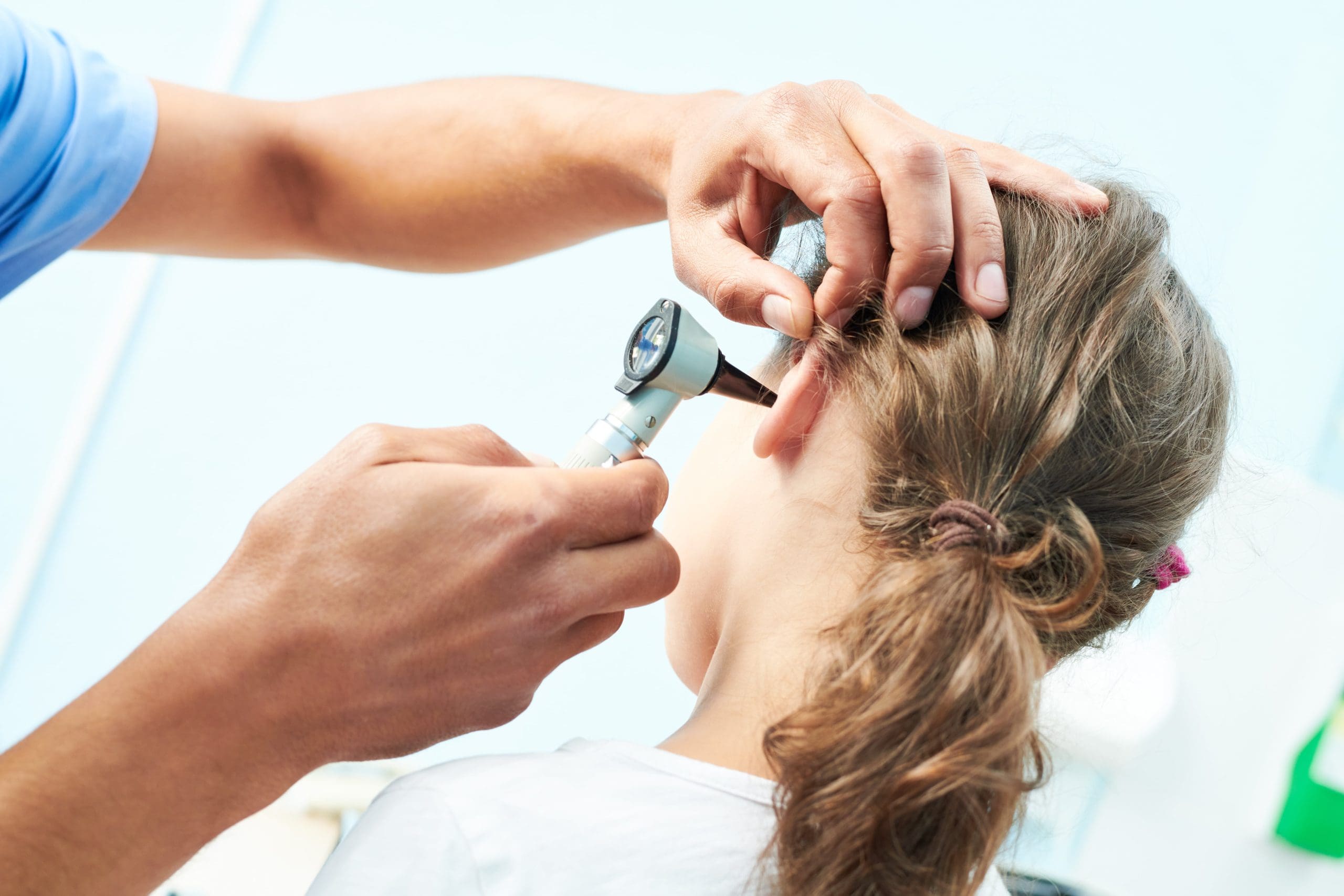 A healthcare professional uses an otoscope to examine a young girl's ear during a medical check-up.