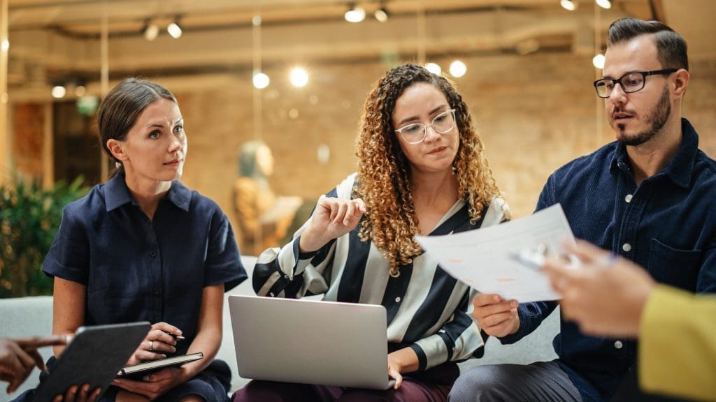 Three professionals in a modern office setting reviewing a document together, reflecting discussion and analysis of employment law changes.