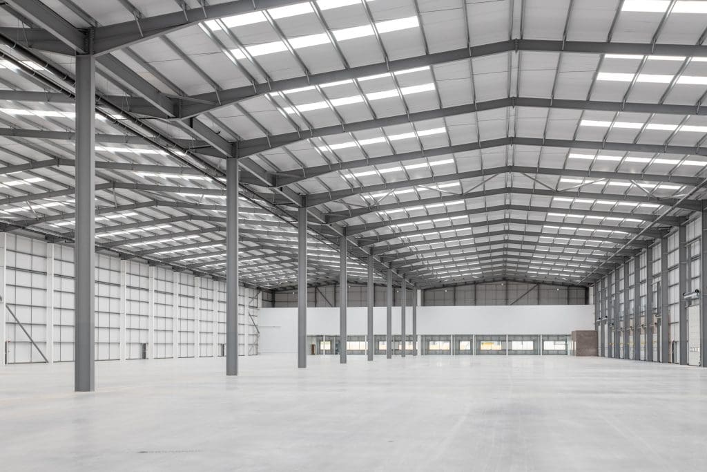 Interior view of a large commercial property warehouse with steel framework and ample natural light from the skylights.