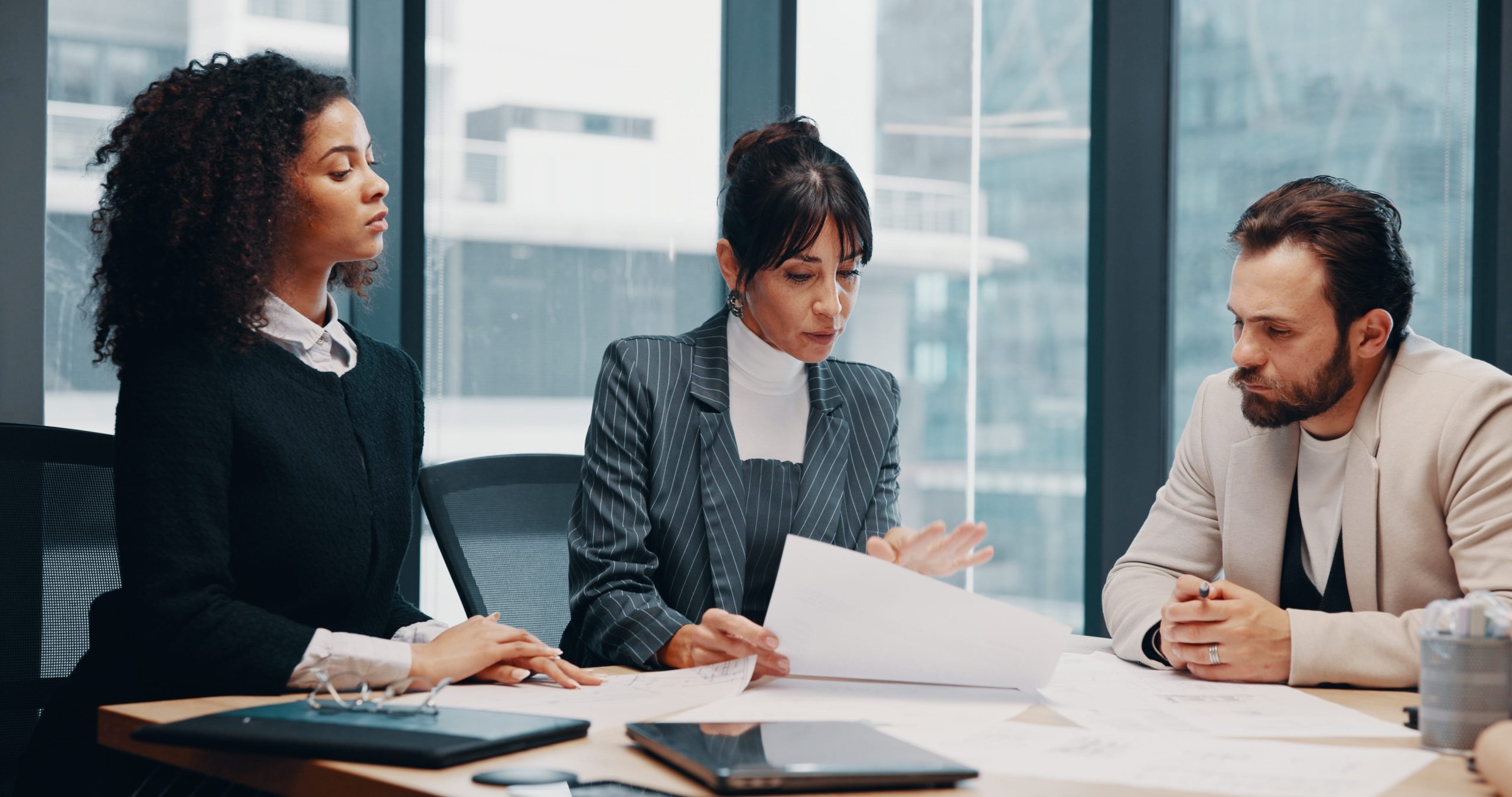 Three professionals reviewing documents in a modern boardroom, discussing compliance and governance matters.